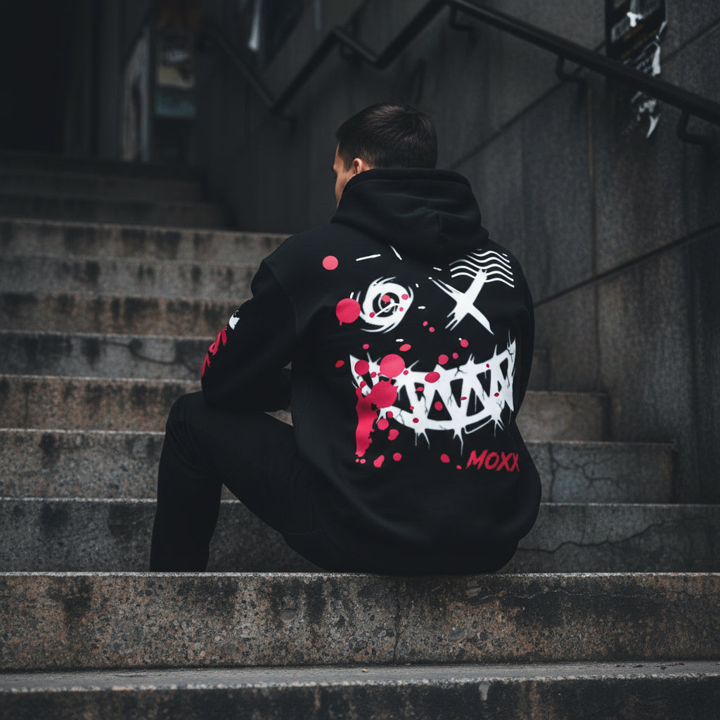 Black hoodie with graphic design and red splashes on a wooden background with 'MOXXapparel.com' text.